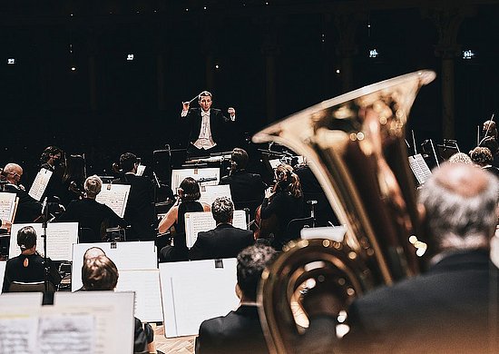 Synfonieorchester von hinten, mit Fokus auf den Dirigenten